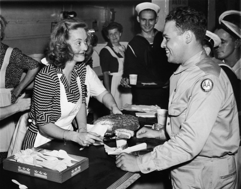 American actor Bette Davis (1908 - 1989) smiles as she serves a slice of cake to US Army private Vazquez while helping Allied troops in the Stage Door Canteen, New York City, July 10, 1943.